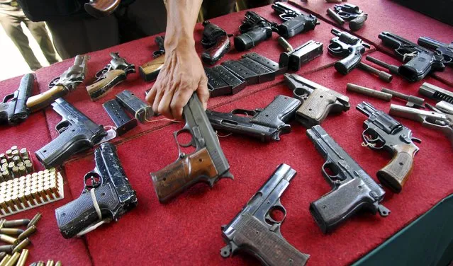 An official holds up confiscated firearms before they are destroyed at the Office of the State Home Foreclosure Confiscated Goods (Rupbasan) in Bandung, December 8, 2014 in this photo taken by Antara Foto. The destroyed firearms were confiscated from 640 cases of narcotics, psychotropic substances, firearms and counterfeit money, according to Antara Foto. (Photo by Agus Bebeng/Reuters/Antara Foto)