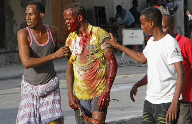 Somalis help a wounded civilian after a car bomb exploded in Mogadishu, Somalia Thursday, March 22, 2018. Somali officials say at least 14 people have been killed and others wounded in a car bomb blast near a hotel in the capital, Mogadishu. Capt. Mohamed Hussein says the explosion occurred near the Weheliye hotel on the busy Makka Almukarramah Road. The road has been a target of attacks in the past by the Somalia-based extremist group al-Shabab. (Photo by Farah Abdi Warsameh/AP Photo)