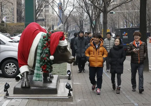 Passersby look at a bull statue decorated with a Santa Claus costume on display in a sidewalk outside a security firm in Seoul, South Korea, Monday, December 15, 2014. (Photo by Ahn Young-joon/AP Photo)