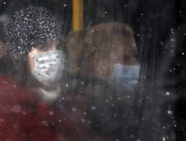 People wearing a face mask to protect against coronavirus sit on a bus in Belgrade, Serbia, Monday, January 11, 2021. A spate of rainy and snowy weather across the Balkans in the past days has left homes and fields flooded, disrupted road and sea traffic and caused power outages. (Photo by Darko Vojinovic/AP Photo)