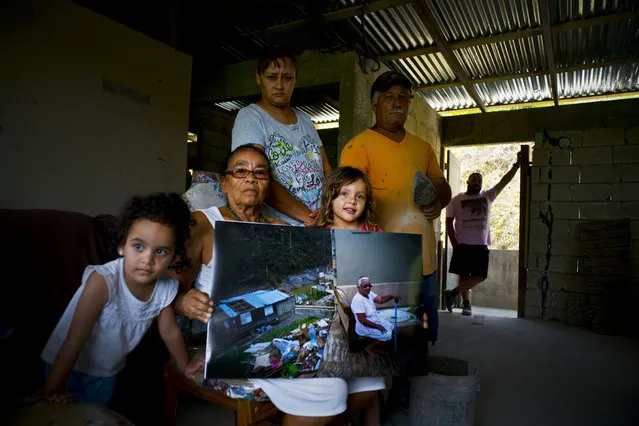 Juana Sostre Vazquez holds a printed photograph of her taken after Hurricane Maria destroyed her home, as she poses with her family inside her new, cinderblock home that has a temporary roof in the San Lorenzo neighborhood of Morovis, Puerto Rico, May 26, 2018. Last year's storm ripped Sostre's wooden home off its foundation in the central mountain highlands. Living on food stamps and Social Security payments, the 69-year-old grandmother rebuilt with the help of her son-in-law and $14,000 in FEMA aid. She said her metal roof is nailed to wooden two-by-fours because she couldn't afford to build stronger and hopes the next hurricane won't send it flying. “The money didn't let us do the roof”, she said. “I'm doing it little by little as I save a couple of dollars”. (Photo by Ramon Espinosa/AP Photo)