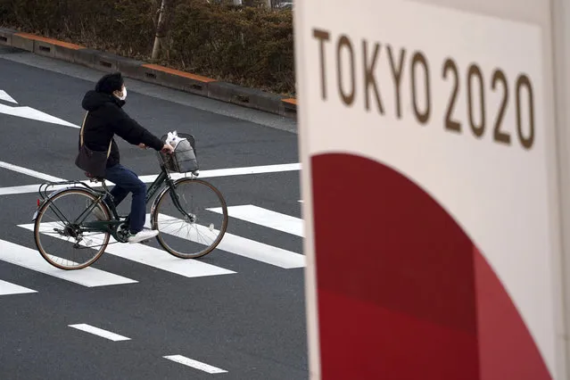 A man wearing a protective mask to help curb the spread of the coronavirus rides a bicycle near a banner of the Tokyo 2020 Olympics in Tokyo Thursday, January 21, 2021. The Japanese capital confirmed more than 1400 new coronavirus cases on Thursday. (Photo by Eugene Hoshiko/AP Photo)