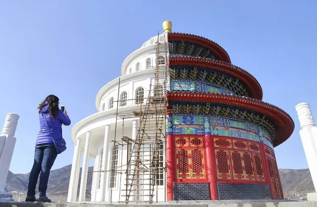 A woman takes pictures with her mobile phone at a building, which is made by half of a replica of the Qinian Hall of the Temple of the Heaven (R) and half of a western building, at a studio for productions of films and television shows on the outskirts of Shijiazhuang, Hebei province, China, December 3, 2015. (Photo by Reuters/Stringer)