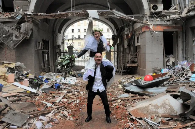 Volunteers Anastasia, top, and Anton pose for a picture in a yard of a destroyed by shelling apartment building during their wedding celebration in Kharkiv, Ukraine, Sunday, April 3, 2022. (Photo by Andrew Marienko/AP Photo)