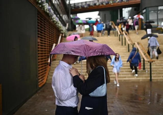 Spectators stand under an umbrella as play on the outer courts is suspended during a rain delay in the first round of matches at Wimbledon on July 4, 2023. (Photo by Dylan Martinez/Reuters)
