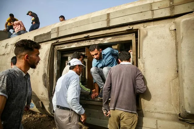 A man climbs out of the hatch of an overturned passenger carriage at the scene of a railway accident in the city of Toukh in Egypt's central Nile Delta province of Qalyubiya on April 18, 2021. (Photo by Ayman Aref/AFP Photo)