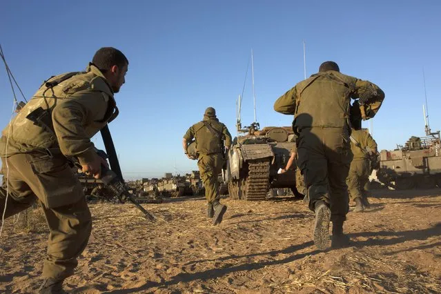 Israeli soldiers run for cover under armored vehicles as a siren sounds warning of incoming rockets fired from Gaza strip in a staging area near the Israeli-Gaza border southern Israel, Saturday, May 15, 2021. (Photo by Maya Alleruzzo/AP Photo)