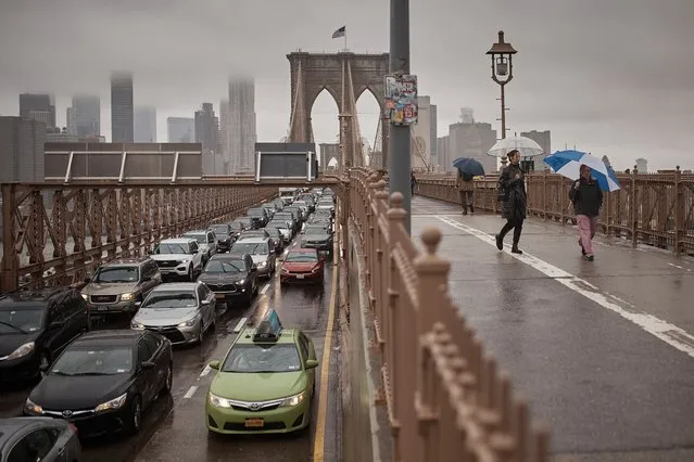 People hold umbrellas as cars move along along Brooklyn Bridge following heavy rains on Friday, September 29, 2023, in New York. (Photo by Andres Kudacki/AP Photo)