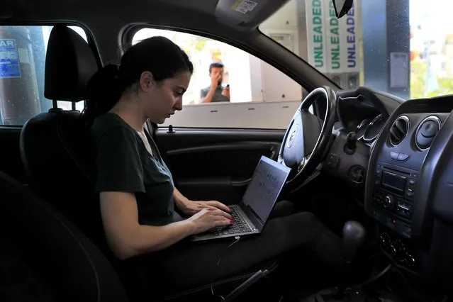 An employee saves time by working on her laptop while waiting on a long queue to fill her car with gasoline in Beirut, Lebanon, Friday, June 25, 2021. Lebanon's caretaker prime minister on Friday granted his approval to allow the financing of fuel imports at a rate higher than the official exchange rate, effectively reducing critical fuel subsidies that have been in place for decades, amid worsening gasoline shortages. (Photo by Hussein Malla/AP Photo)
