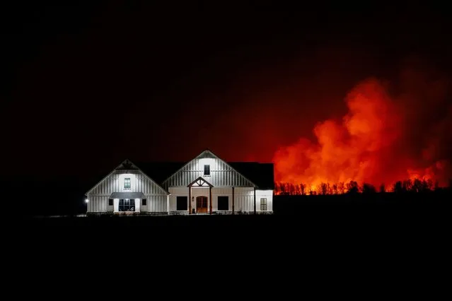 A wildfire that prompted evacuations burns in the distance behind a home outside of Shattuck, Oklahoma, U.S. February 27, 2024. (Photo by Nick Oxford/Reuters)