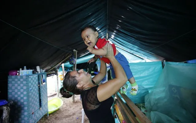 In this Tuesday, February 28, 2017 photo, FARC rebel Jerly Suarez holds up her 9-month-old son Dainer inside her tent at a rebel camp in a demobilization zone in La Carmelita, in Colombia's southwestern Putumayo state. In La Carmelita, where 500 guerrillas are expected to turn over their weapons by June 1, women speak of both the arduous conditions in which they have begun their new lives as mothers and their hopes for raising children in a time of peace. (Photo by Fernando Vergara/AP Photo)
