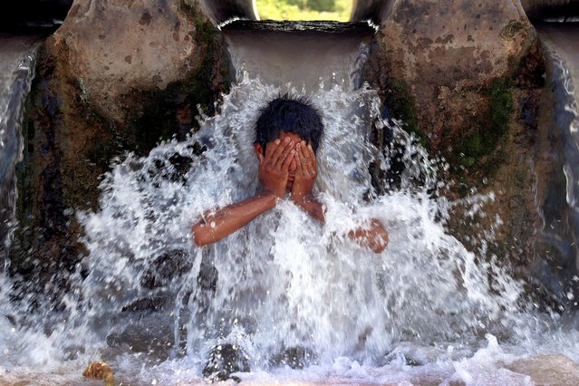 A boy cools off under a water pipe from a canal during a hot summer day on the outskirts of Peshawar, Pakistan, on May 28, 2024. (Photo by Fayaz Aziz/Reuters)