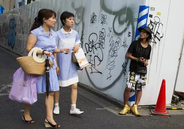 Women walk along a street as a man leans against a graffiti-covered wall in the trendy Harajuku district in Tokyo, July 17, 2015. (Photo by Thomas Peter/Reuters)