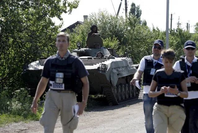 Members of the Organisation for Security and Co-operation in Europe (OSCE) walk past an armoured personnel carrier (APC) of the self-proclaimed Donetsk People's Republic forces outside the village of Novolaspa in Donetsk region, Ukraine, July 19, 2015. (Photo by Alexander Ermochenko/Reuters)