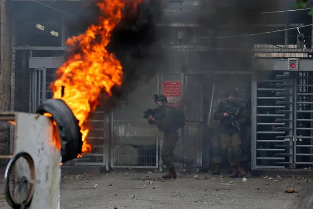 Israeli soldiers run as a tire burns during a Palestinian protest over a U.S. decision on Jewish settlements, in Hebron in the Israeli-occupied West Bank on December 9, 2019. (Photo by Mussa Qawasma/Reuters)