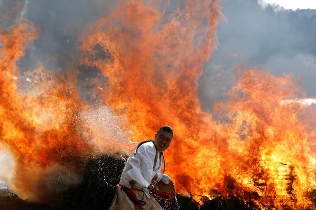 A Buddhist monk splashes water on a bonfire at the fire-walking festival, called Hiwatari Matsuri in Japanese, at Mt.Takao in Tokyo, Japan, March 13, 2022. About 1,500 Japanese worshipers walk barefoot with Buddhist monks over coals at the annual festival praying for the safety of themselves, to overcome the coronavirus disease (COVID-19) pandemic and for peace in the world, Takao-san Yakuo-in Buddhist temple said. (Photo by Kim Kyung-Hoon/Reuters)