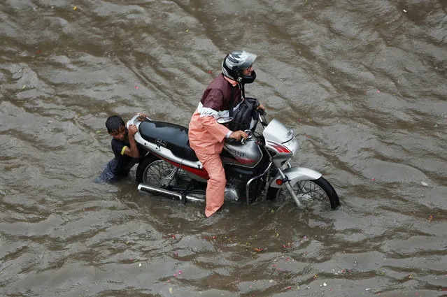 A man drags his motorcycle through a flooded road after a heavy rainfall in Ahmedabad, India July 3, 2017. (Photo by Amit Dave/Reuters)