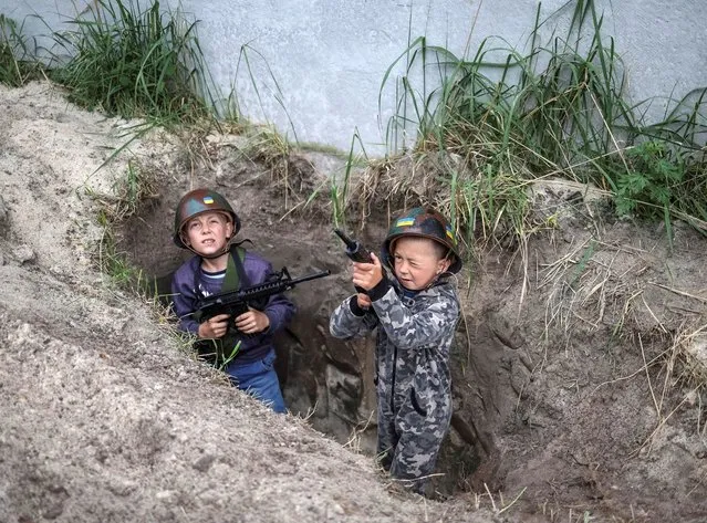 Ukrainian children Andrii, 12 and Valentyn, 6, stand in a foxhole as they play Ukrainian military near their houses, amid Russia's invasion, in the village of Stoianka, in Kyiv region, Ukraine on May 22, 2022. (Photo by Gleb Garanich/Reuters)