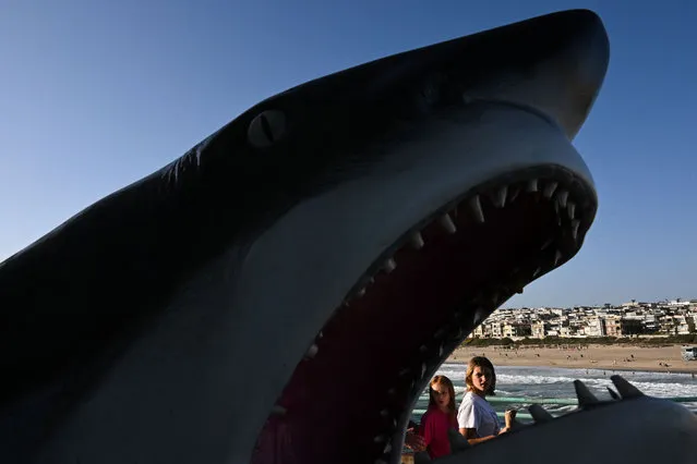 People carry ice cream cones as they walk past a statue of a great white shark on the Manhattan Beach pier on June 14, 2022 in Manhattan Beach, California. The US Federal Reserve is poised to raise borrowing costs on June 15 amid the troubling acceleration of inflation, with the only question being whether officials will opt for the biggest hike in nearly three decades or a smaller step up. (Photo by Patrick T. Fallon/AFP Photo)