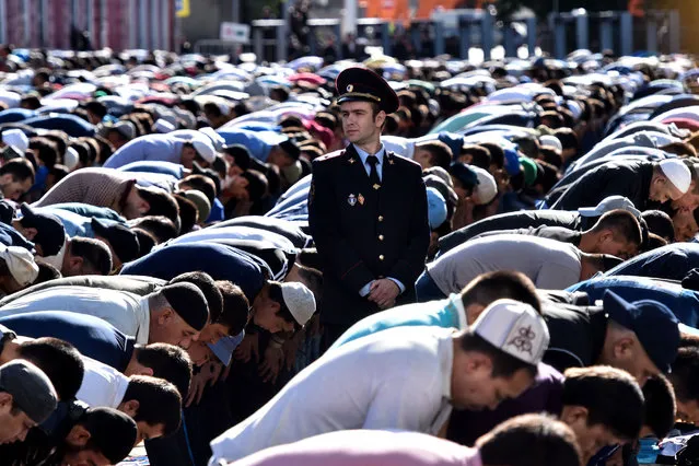 A police officer stands among Russian Muslims praying outside the central mosque in Moscow on July 5, 2016, during celebrations of Eid al-Fitr marking the end of the fasting month of Ramadan. (Photo by Kirill Kudryavtsev/AFP Photo)