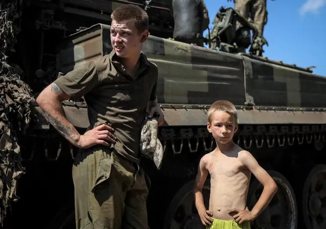A local boy stands with a Ukrainian serviceman near a military vehicle not far from the front line, amid Russia's attack on Ukraine, in the Donbas region, Ukraine on July 17, 2022. (Photo by Gleb Garanich/Reuters)