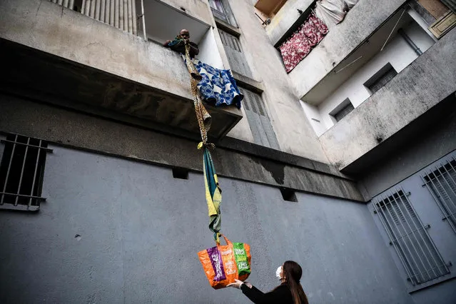 A resident of the White House estate, a private condominium of 226 mostly unsanitary dwellings, collects food offered by neighbours from his balcony, using a rope made with blankets, on March 31, 2020, in Marseille, southern France, on the fifteenth day of a lockdown aimed at curbing the spread of the COVID-19 (novel coronavirus). (Photo by Anne-Christine Poujoulat/AFP Photo)