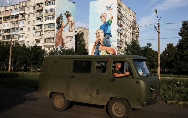 Ukraine servicemen drive past a graffiti of a family on damaged buildings in Bakhmut, as Russia's invasion of Ukraine continues, in Donetsk region, Ukraine on August 14, 2022. (Photo by Nacho Doce/Reuters)