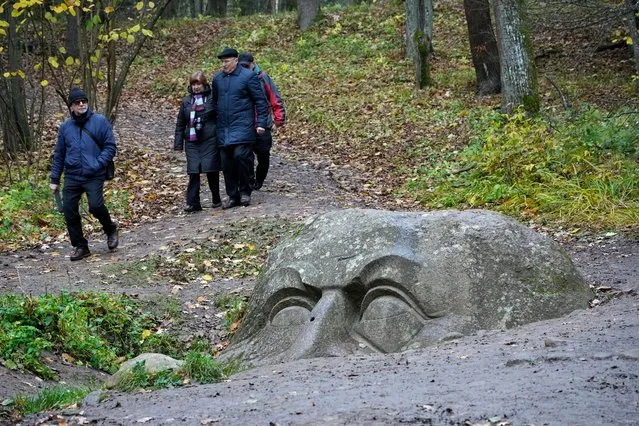 People walk past a huge head carved out of stone and buried in the ground in Sergievka park outside St. Petersburg, Russia, Friday, October 21, 2022. The sculpture of an unknown man, carved in a giant granite boulder, is from the 19th century but the history of its appearance in the park is unknown. (Photo by Dmitri Lovetsky/AP Photo)