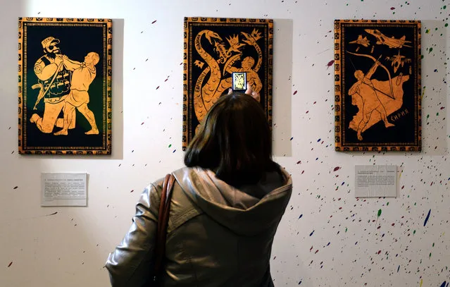 A visitor takes photos of the paintings during the “12 Labours of Putin” art exhibition on October 6, 2014 marking the 60th birthday of Russia's President Vladimir Putin at the design workshop in Moscow. (Photo by Vasily Maximov/AFP Photo)