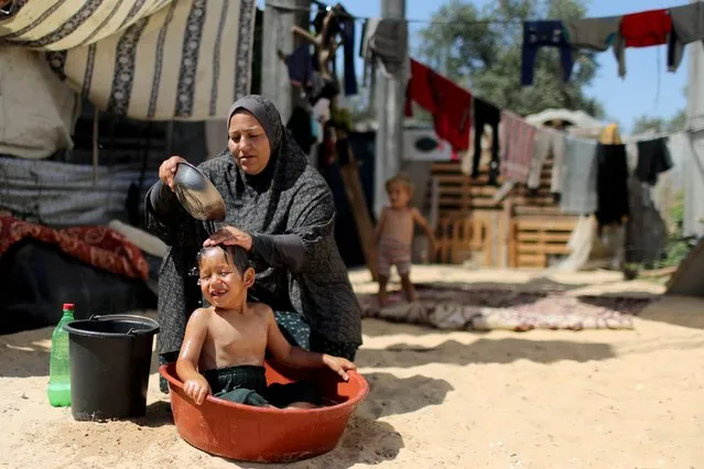 A Palestinian woman bathes her son in a plastic basin on a hot day outside their dwelling in the northern Gaza Strip on July 15, 2020. (Photo by Mohammed Salem/Reuters)