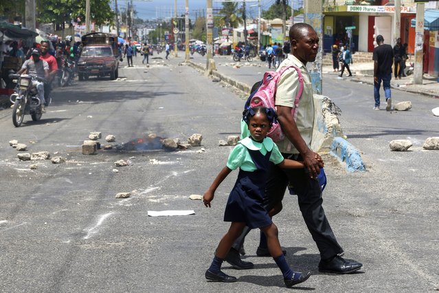 Pedestrians cross a road blocked off with stones by protestors during a demonstration demanding the resignation of the transitional presidential council, in Port-au-Prince, Haiti, March 26, 2025. (Photo by Odelyn Joseph/AP Photo)