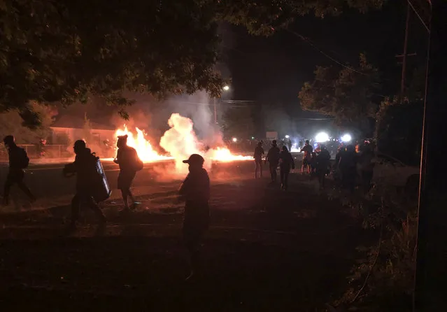 Flames rise from a street after a liquid had been spread and lit, Saturday, September 5, 2020, during protests in Portland, Ore. Some protesters, at, left, move back as police, at background right, advance. (Photo by Andrew Selsky/AP Photo)