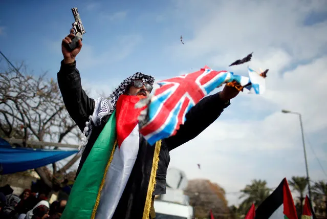 A Palestinian demonstrator holds a pistol as he burns representations of Israeli and British flags during a protest against a U.S. decision to cut aid, in Gaza City January 29, 2018. (Photo by Mohammed Salem/Reuters)