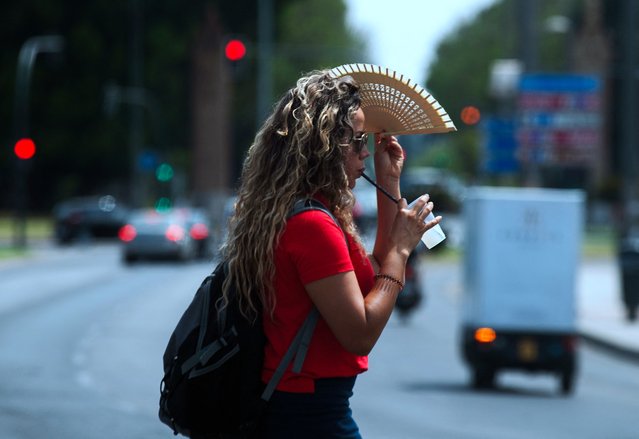 A woman uses a fan to protect herself from the sun in Seville, on June 18, 2025 as a heatwave hits Spain. (Photo by Cristina Quicler/AFP Photo)
