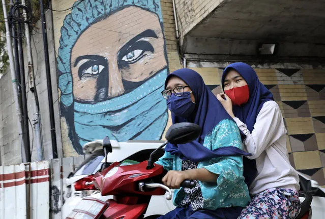 Women wearing masks as a precaution against the coronavirus ride a motorbike past a large COVID-19-themed mural in Jakarta, Indonesia, Friday, October 2, 2020. (Photo by Dita Alangkara/AP Photo)