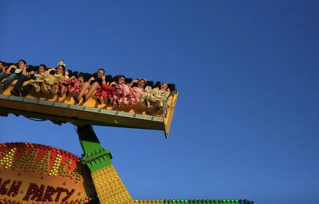 Children, wearing typical Sevillana outfits, sit in a ride at the amusement park of the traditional Feria de Abril (April fair) in the Andalusian capital of Seville, southern Spain April 18, 2013. (Photo by Marcelo del Pozo/Reuters)