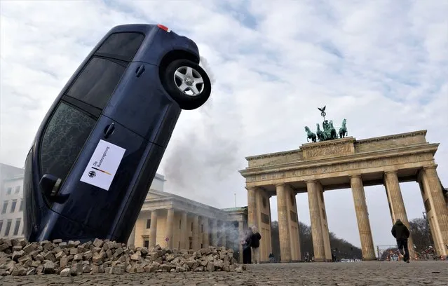 A SUV is piled into the ground in front of Berlin's landmark Brandenburg Gate during a protest “stop crashing the climate” by Greenpeace in Berlin, Germany on March 22, 2023. (Photo by Michele Tantussi/Reuters)