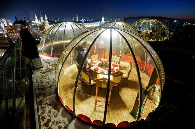 A waiter sets a table inside a transparent pod offered for private Christmas meals with backdrop of the Kremlin and Red Square on the rooftop of Ritz-Carlton hotel in Moscow, Russia on December 8, 2020. (Photo by Maxim Shemetov/Reuters)