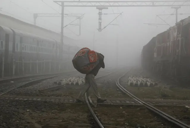 A man carries blankets as he crosses railway tracks on a foggy and cold winter morning in the northern Indian city of Allahabad December 29, 2014. (Photo by Jitendra Prakash/Reuters)