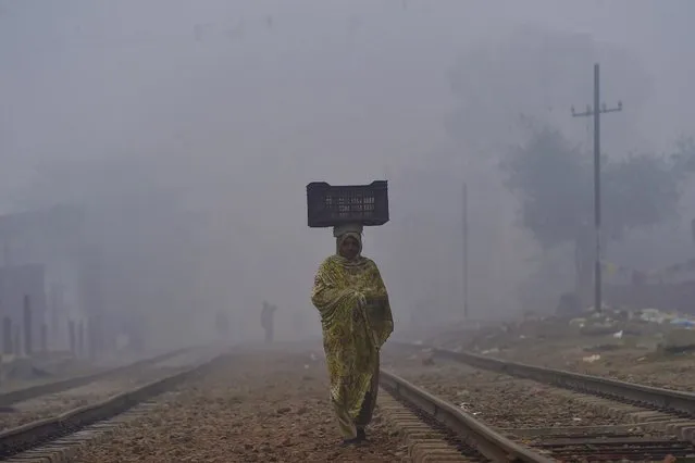 A woman carries a basket on her head while walking on a railway track during smog and fog conditions, in Lahore on December 27, 2020.  (Photo by Arif Ali/AFP Photo)