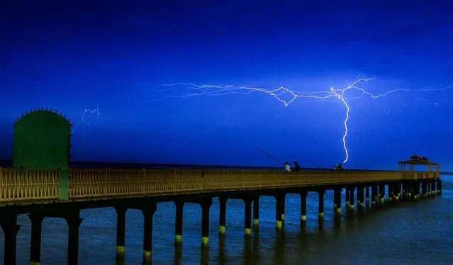 Lightning flashes over people fishing on the coast near Kuwait City, Kuwait, 29 October 2015. (Photo by Raed Qutena/EPA)