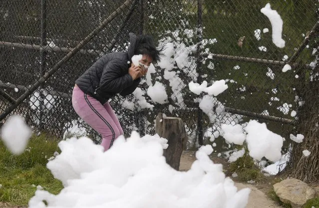 A woman tries to avoid clouds of toxic foam rising from the Balsillas River in the Los Puentes neighborhood in Mosquera, Colombia, Wednesday, April 27, 2022. According to local authorities, the white toxic foam is caused in part by untreated sewage mixing with chemicals found in household detergents. (Photo by Fernando Vergara/AP Photo)