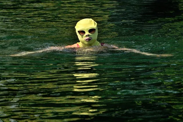 A woman wearing a sun protection headgear and wearing a sun glasses swims to cool off on a sweltering day at an urban waterway in Beijing, Monday, July 10, 2023. Rescuers were looking Monday for several people missing in a landslide triggered by torrential rains while employers across much of China were ordered to limit outdoor work due to scorching temperatures as the country struggled with heat, flooding and drought. (Photo by Andy Wong/AP Photo)