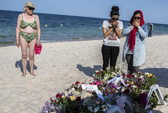 Women pray near bouquets of flowers laid on the beach of the Imperial Marhaba resort, which was attacked by a gunman, in Sousse, Tunisia, June 28, 2015. (Photo by Zohra Bensemra/Reuters)