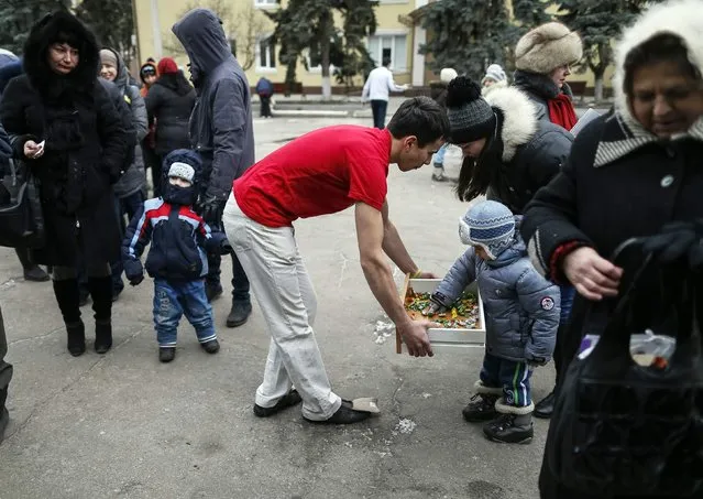 A volunteer distributes candy to refugees from eastern Ukraine as they stand in a queue to receive food donated to a volunteer centre in Slaviansk February 7, 2015. (Photo by Gleb Garanich/Reuters)