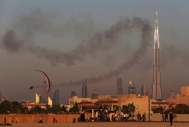 A man in a powered parachute sprays smoke over a crowd with the Burj Khalifa, the world's tallest building, in the background in Dubai, United Arab Emirates, on Friday, January 8, 2016. (Photo by Jon Gambrell/AP Photo)