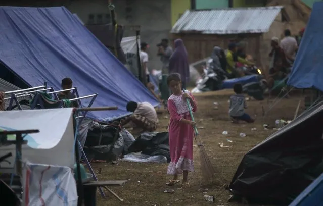 A girl sweeps at a temporary shelter after being displaced by Sunday's earthquake in North Lombok, Indonesia, Wednesday, August 8, 2018. Aid has begun reaching isolated areas of the Indonesian island struggling after an earthquake killed over 100 people as rescuers intensify efforts to find those buried in the rubble. (Photo by Tatan Syuflana/AP Photo)