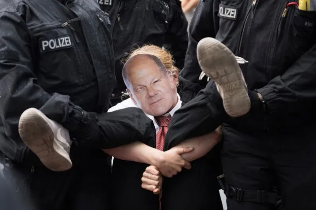 Police officers carry a participant wearing a mask with the likeness of Scholz off the street in front of the main train station during a protest march of the climate protection group “Last Generation” in Berlin on September 13, 2023. The protest march is the beginning of new blockades and protest in the capital. (Photo by Sebastian Christoph Gollnow/dpa)