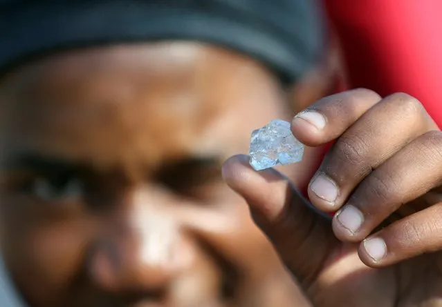 A man shows an unidentified stone as fortune seekers flock to the village after pictures and videos were shared on social media showing people celebrating after finding what they believe to be diamonds, in the village of KwaHlathi outside Ladysmith, in KwaZulu-Natal province, South Africa, June 14, 2021. (Photo by Siphiwe Sibeko/Reuters)