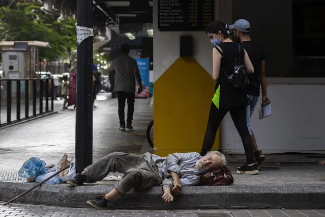 A woman looks to a homeless Lebanese man who sleeps on the ground at Hamra trade street, in Beirut, Lebanon, Friday, July 17, 2020. With virtually no national welfare system, Lebanon’s elderly are left to fend for themselves amid their country’s economic turmoil. In their prime years, they survived 15 years of civil war that started in 1975 and bouts of instability. Now, in their old age, many have been thrown into poverty by one of the world’s worst financial crises in the past 150 years. (Photo by Hassan Ammar/AP Photo)
